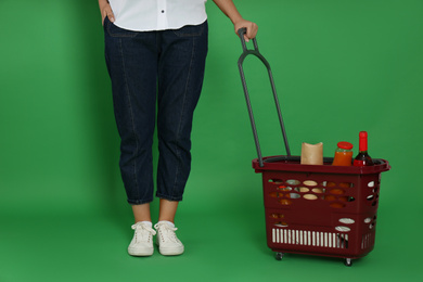 Photo of Woman with shopping basket full of different products on green background, closeup