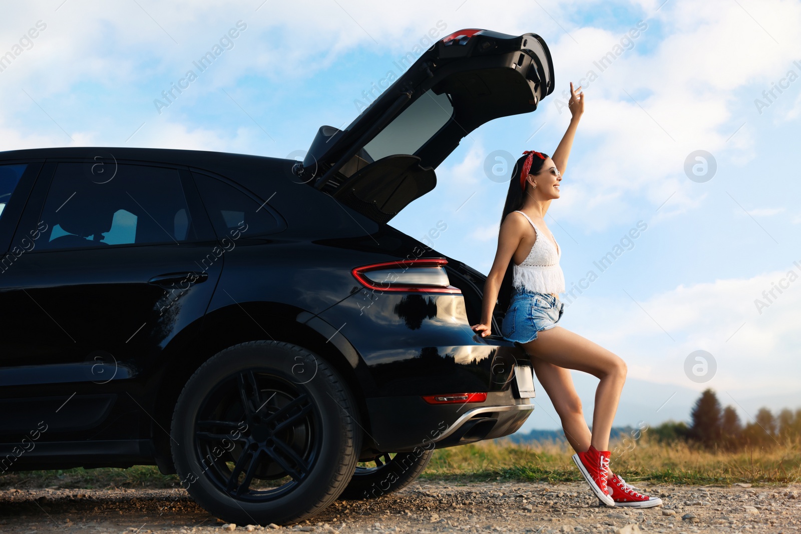 Photo of Happy woman sitting in trunk of modern car on roadside outdoors