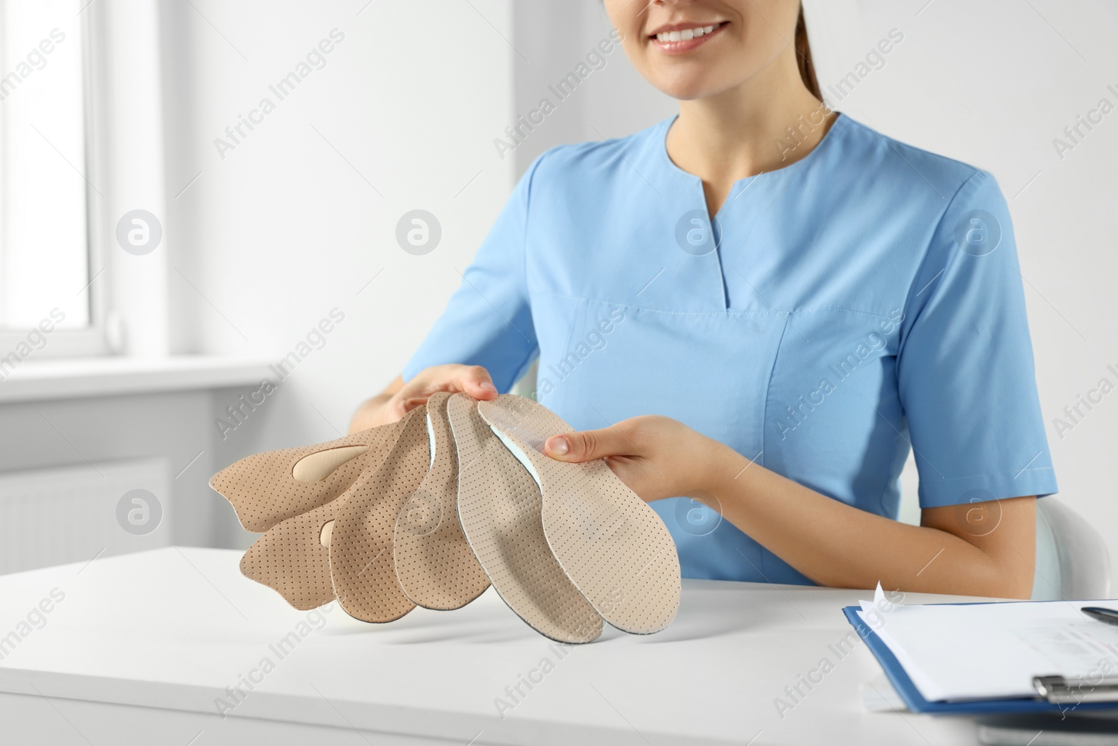 Photo of Female orthopedist showing insoles at table in hospital, closeup