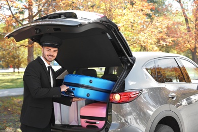 Photo of Young driver loading suitcases into car trunk outdoors