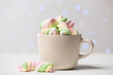 Ceramic cup with colorful marshmallows on white table against blurred lights