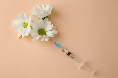 Photo of Medical syringe and beautiful chrysanthemum flowers on beige background, above view