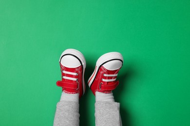 Photo of Little child in stylish red gumshoes on green background, top view