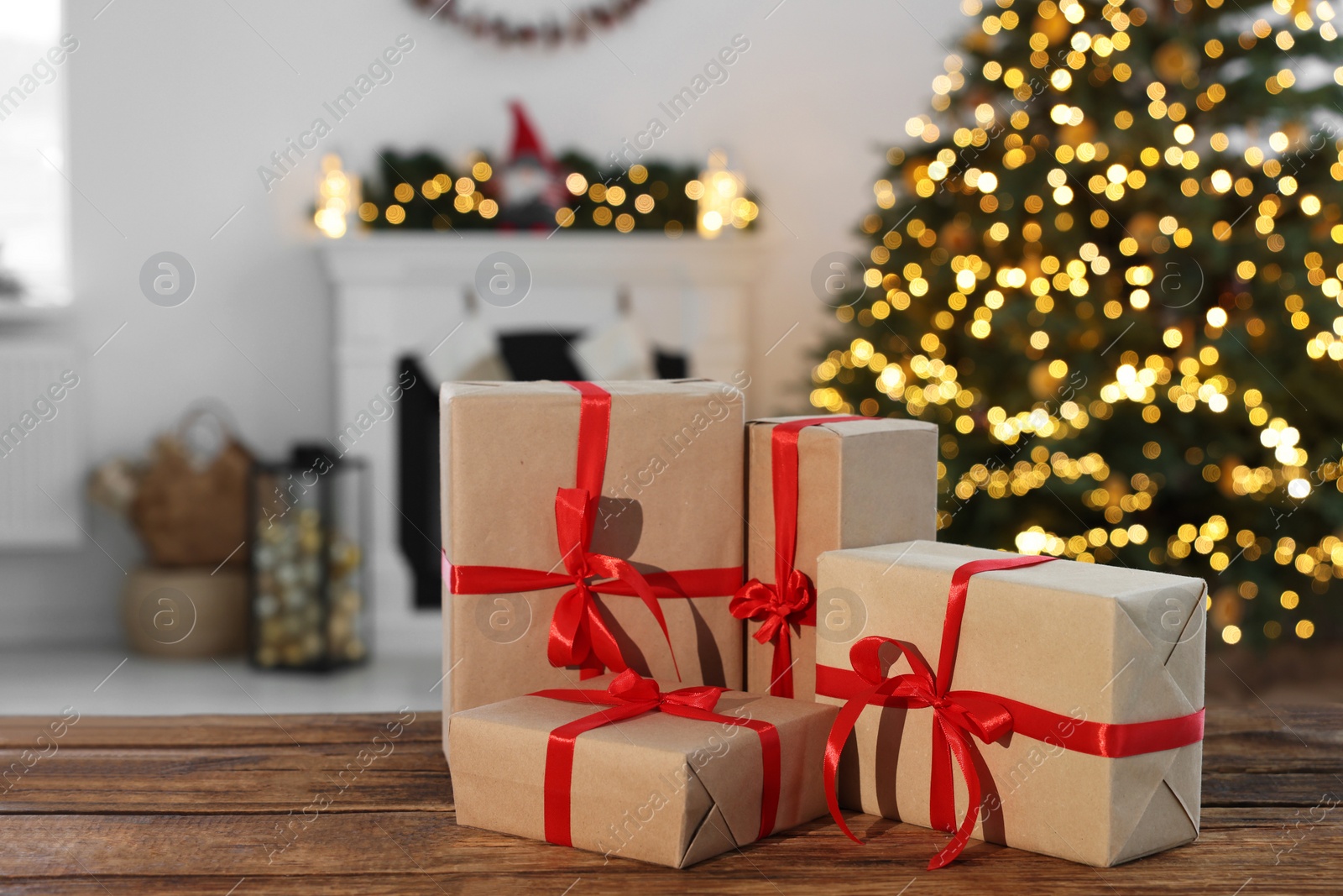 Photo of Many different gift boxes on wooden table against blurred festive lights in living room, space for text. Christmas presents