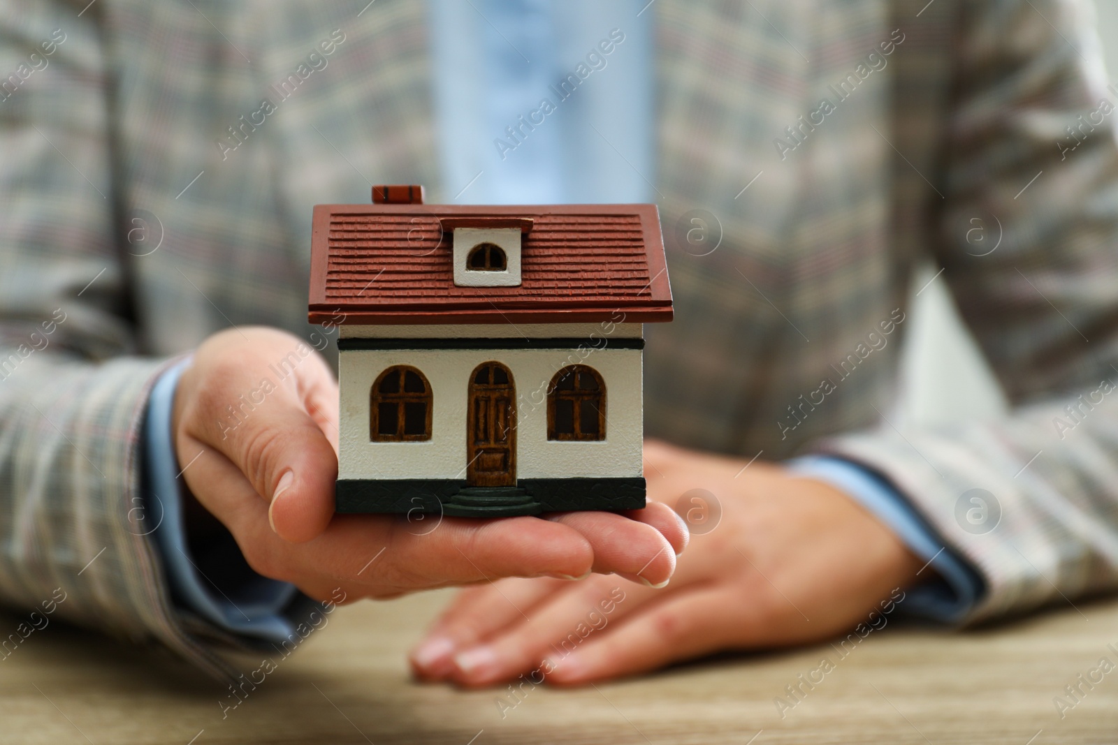 Photo of Real estate agent holding house model at wooden table, closeup