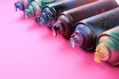 Many spray paint cans on pink background, closeup. Space for text
