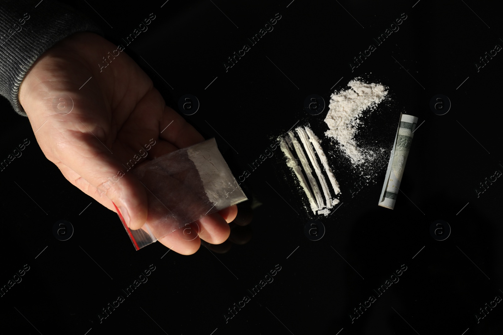 Photo of Drug addiction. Man with cocaine and rolled dollar banknote at black table, top view