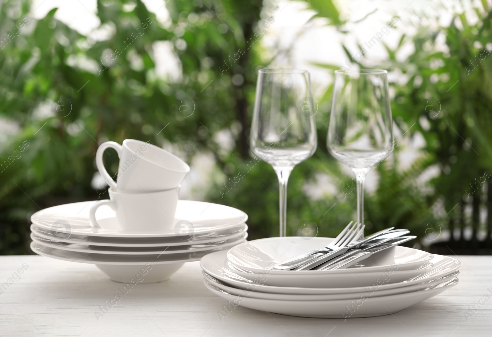 Photo of Set of clean dishware, cutlery and wineglasses on white table against blurred background