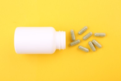 Photo of Jar with vitamin capsules on yellow background, top view