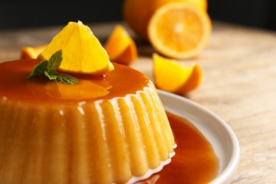 Photo of Delicious pudding with caramel, orange and mint on wooden table, closeup