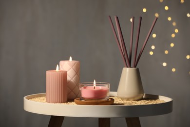 Photo of Burning candles and reed diffuser on table against grey background