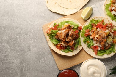 Photo of Delicious tacos with vegetables, meat and sauce on grey textured table, flat lay. Space for text