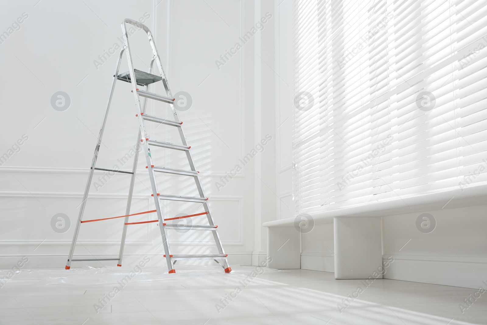 Photo of Metal stepladder on floor covered with plastic in empty room, space for text