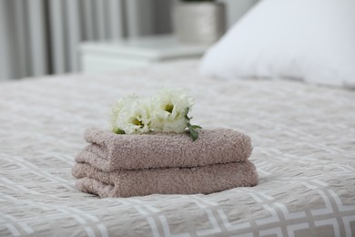 Photo of Stack of clean towels and Eustoma flowers on bed indoors