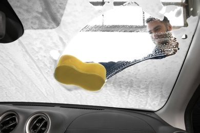 Worker cleaning automobile windshield with sponge at car wash, view from inside