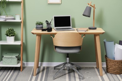 Workplace with laptop, stationery on desk and chair in home office