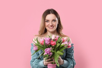 Happy young woman with bouquet of beautiful tulips on pink background