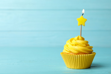 Photo of Delicious birthday cupcake with cream and burning candle on blue wooden background. Space for text