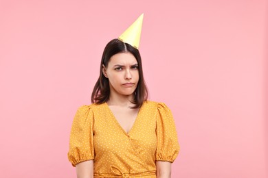 Sad young woman in party hat on pink background