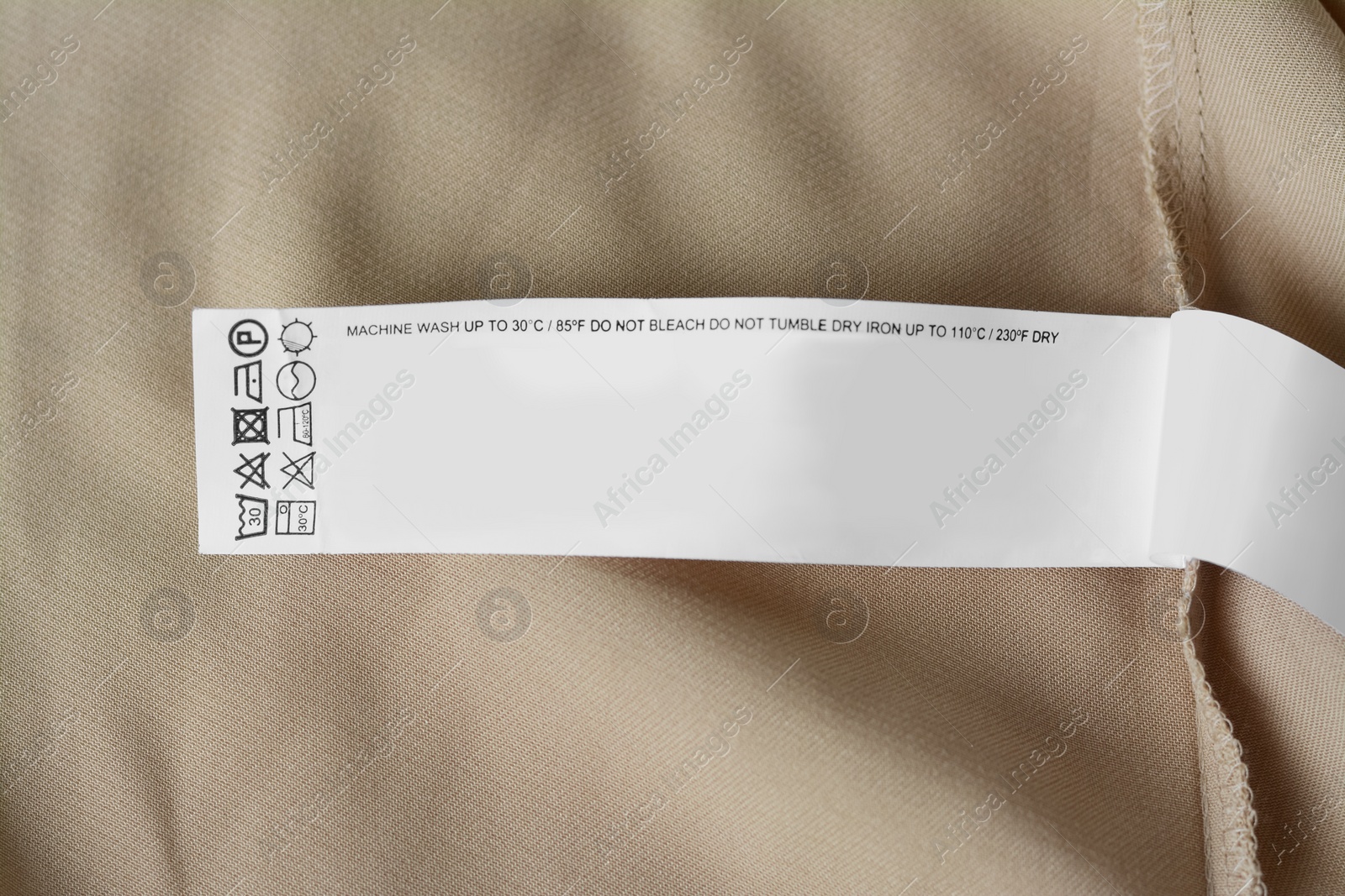 Photo of White clothing label with care information on beige garment, top view