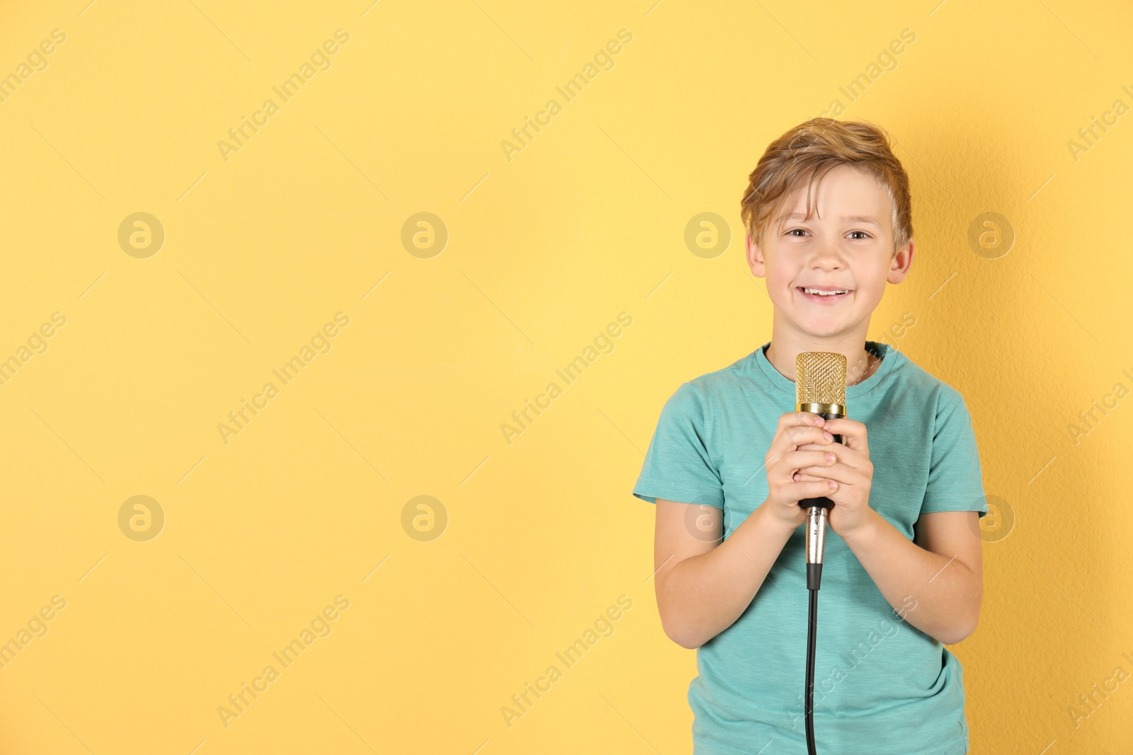 Photo of Cute boy with microphone on color background. Space for text