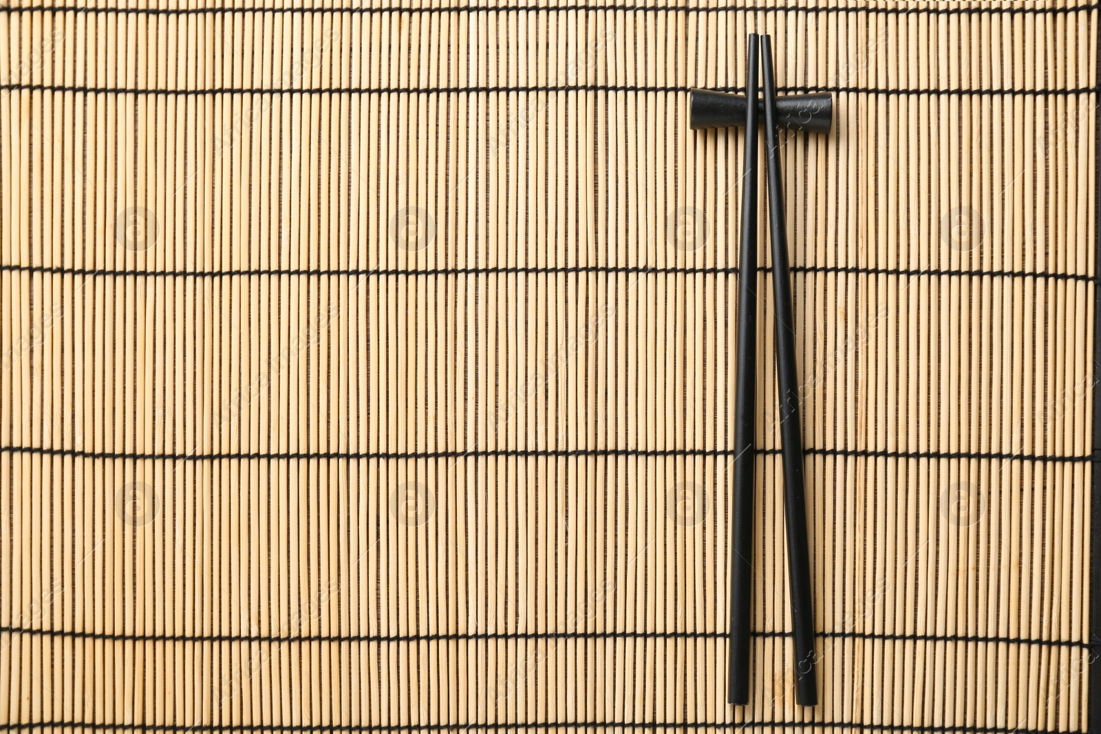 Photo of Pair of black chopsticks with rest on bamboo mat, top view. Space for text