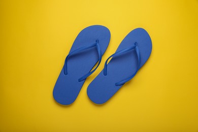 Stylish blue flip flops on yellow background, top view