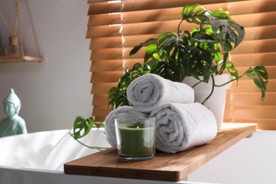 Photo of Soft towels, burning candle and green plant on bathtub in room. Interior design