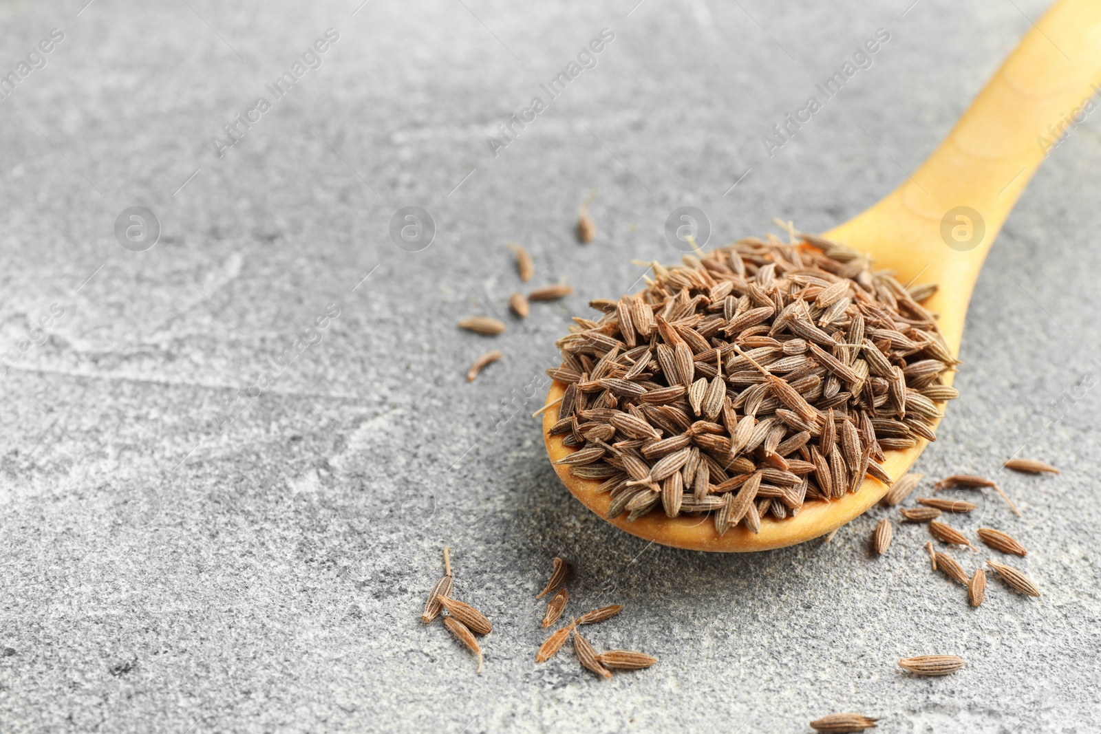 Photo of Spoon with caraway seeds on grey table, closeup. Space for text