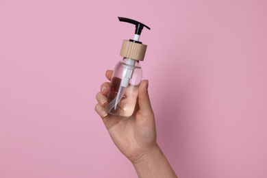 Woman holding bottle of cosmetic product on pink background, closeup