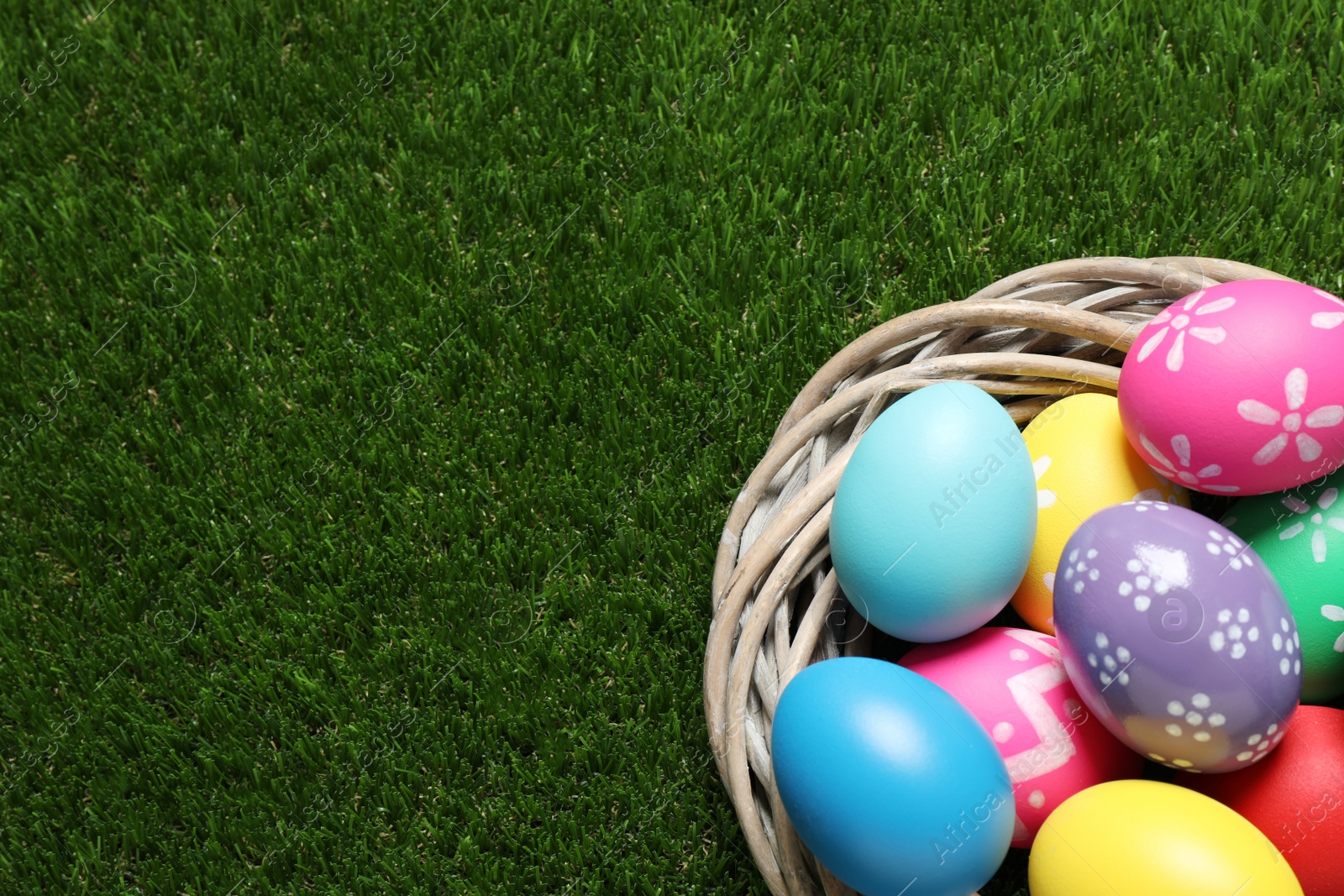 Photo of Colorful Easter eggs in decorative nest on green grass, top view. Space for text