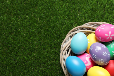 Photo of Colorful Easter eggs in decorative nest on green grass, top view. Space for text