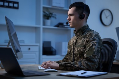 Photo of Military service. Young soldier in headphones working at table in office at night