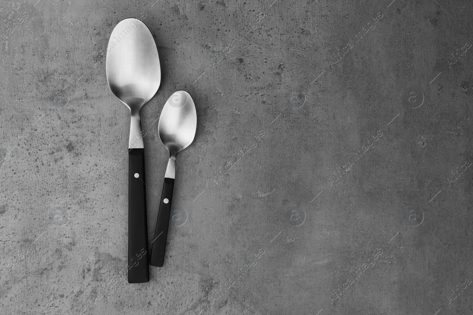 Photo of Clean empty table spoons on grey background, top view. Space for text