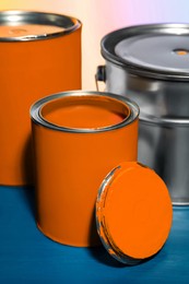 Photo of Cans and bucket of orange paint on blue wooden table against color background