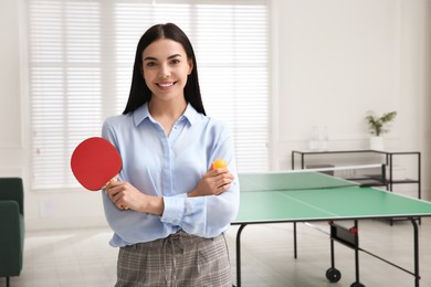 Business woman with tennis racket and ball near ping pong table in office. Space for text