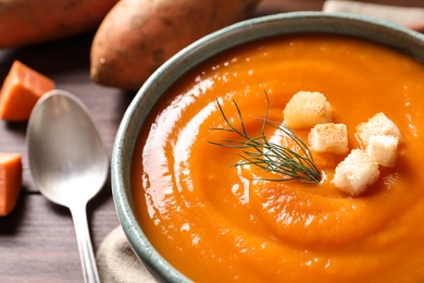 Photo of Bowl of tasty sweet potato soup on table, closeup