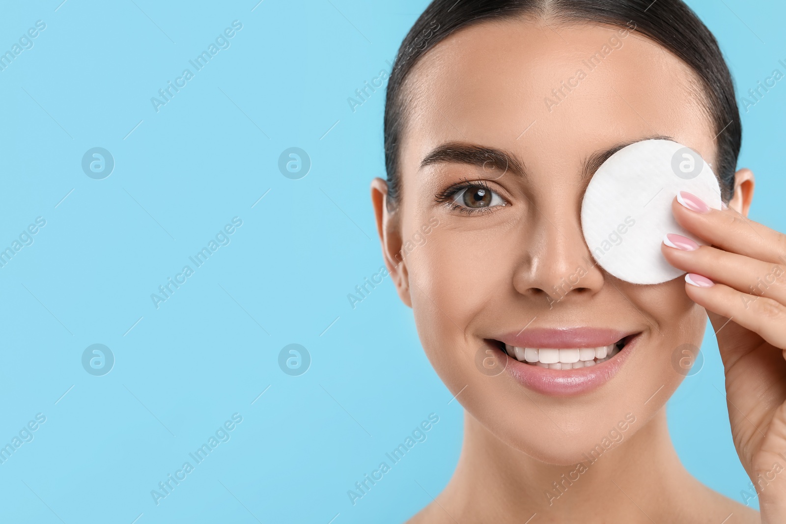 Photo of Beautiful woman removing makeup with cotton pad on light blue background, closeup. Space for text