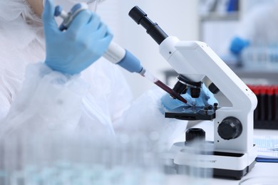 Photo of Scientist dripping sample onto glass slide while working with microscope in laboratory, closeup