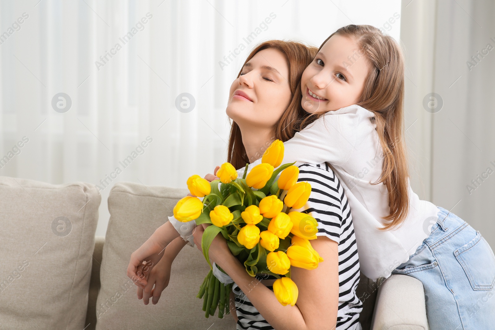 Photo of Mother and her cute daughter with bouquet of yellow tulips at home. Space for text