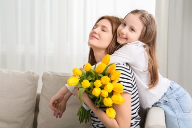 Mother and her cute daughter with bouquet of yellow tulips at home. Space for text