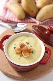 Photo of Tasty potato soup with croutons and rosemary in ceramic pot on white table, closeup