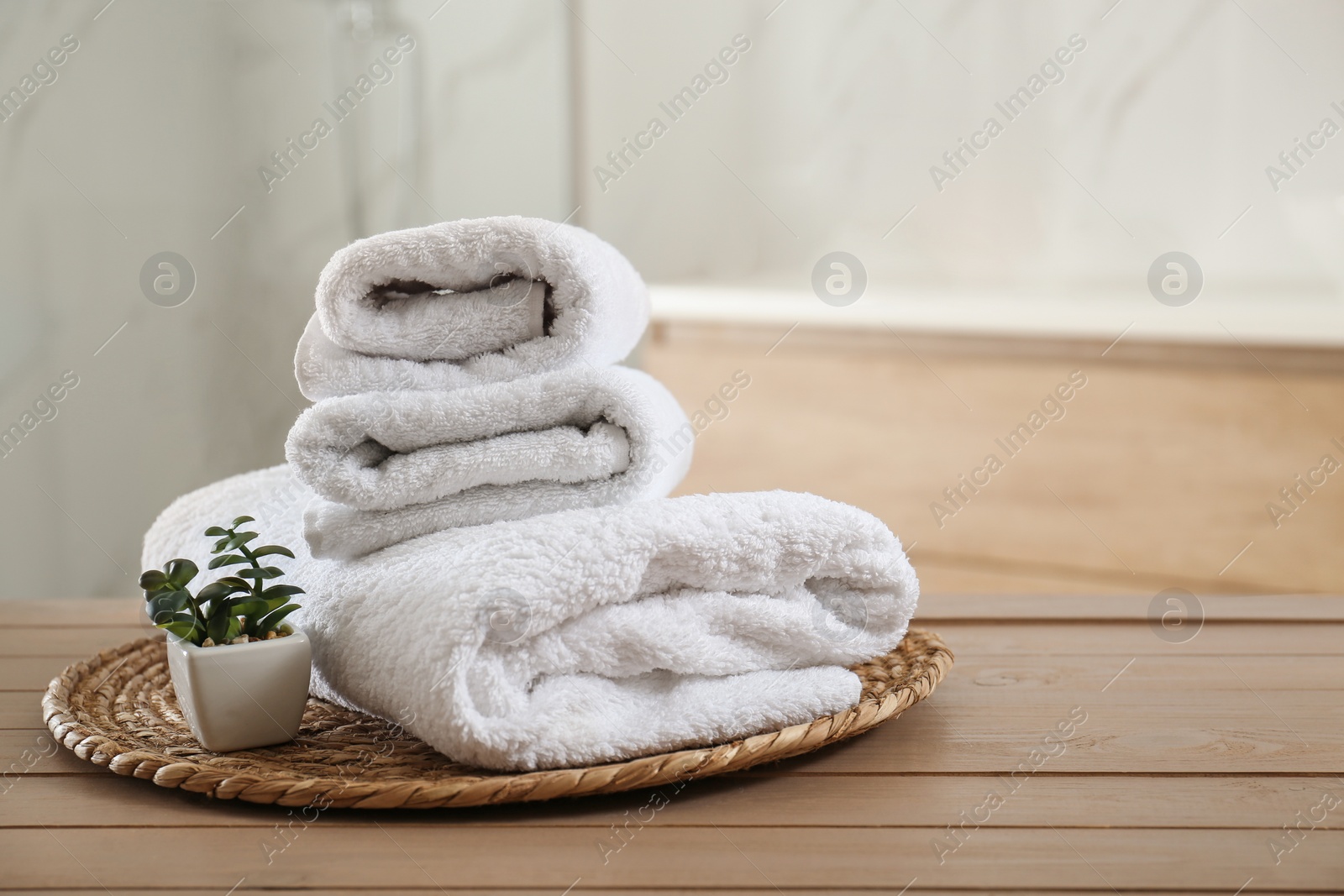 Photo of Clean folded towels and plant on wooden table in bathroom. Space for text