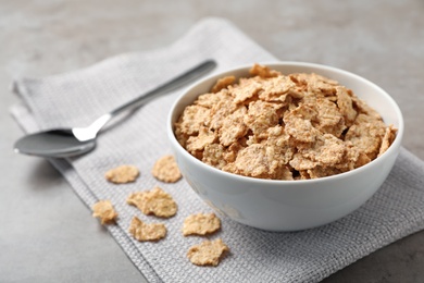 Photo of Bowl with cornflakes on gray table. Whole grain cereal for breakfast