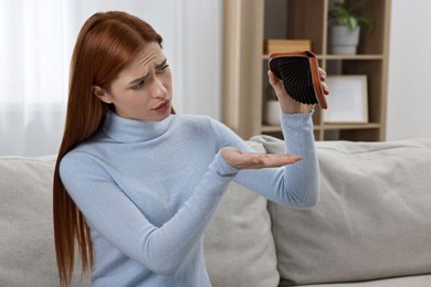 Upset woman with empty wallet on sofa indoors