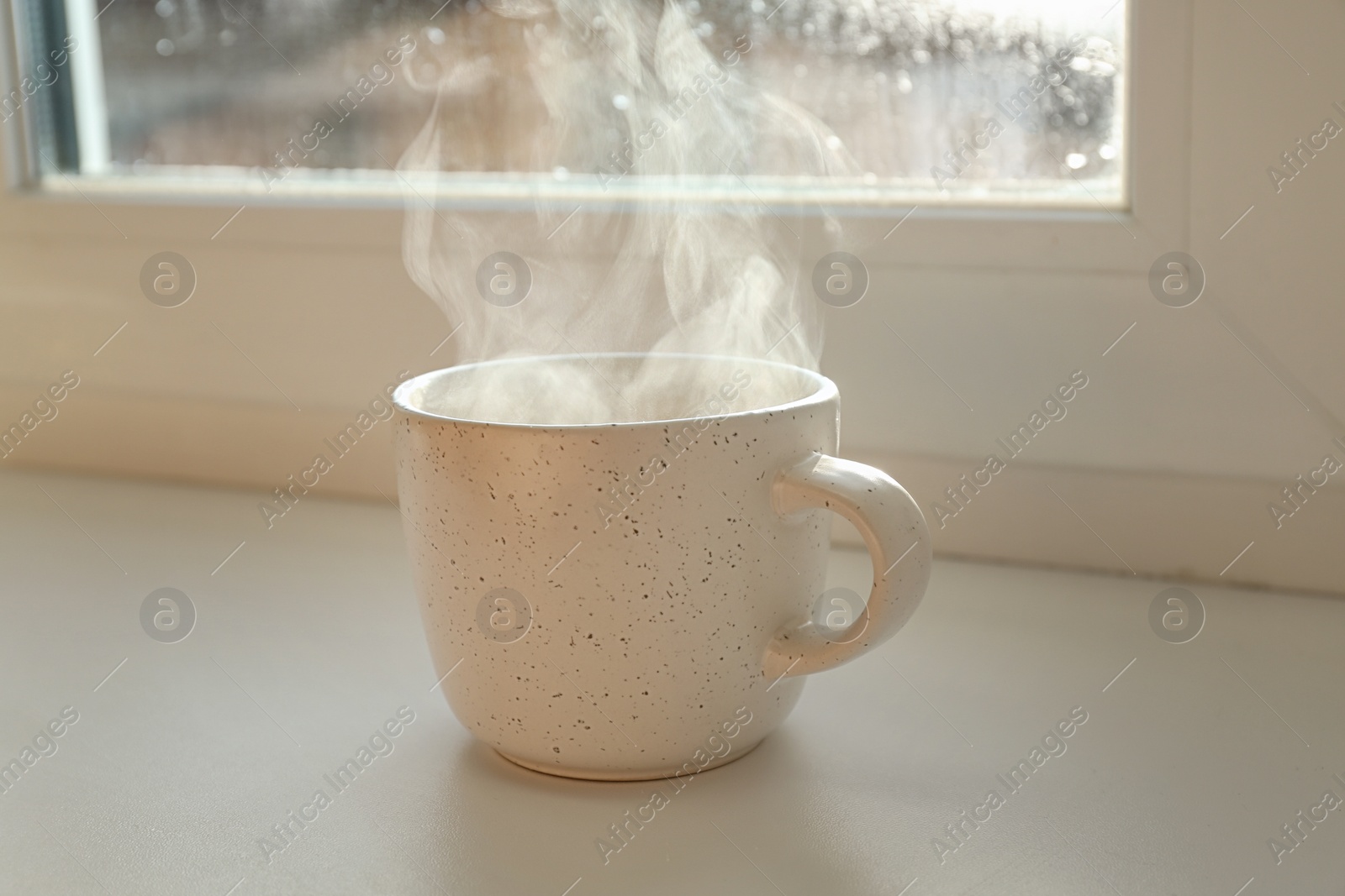 Photo of Cup of hot drink near window on rainy day