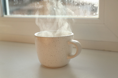 Photo of Cup of hot drink near window on rainy day
