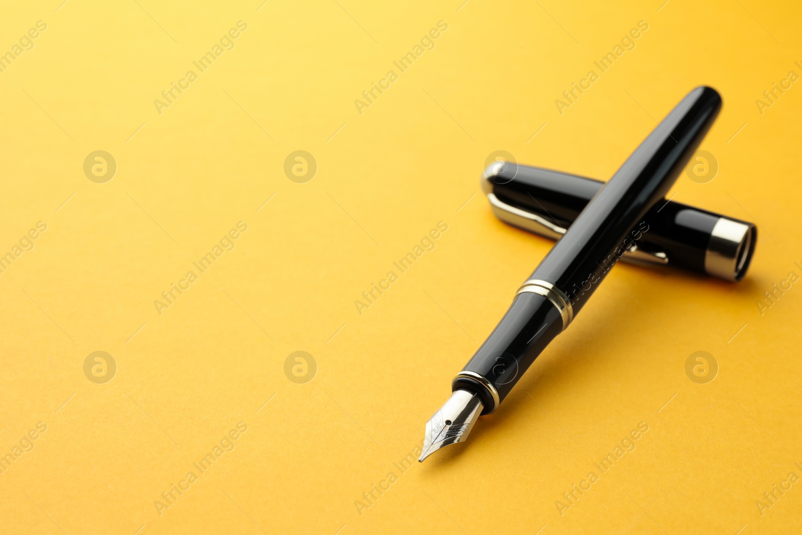 Photo of Stylish fountain pen with cap on yellow background. Space for text