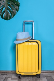 Photo of Bright yellow suitcase with hat and tropical leaf near color wall indoors