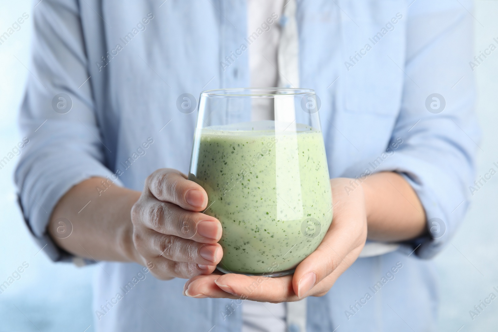 Photo of Woman holding green buckwheat smoothie on light blue background, closeup